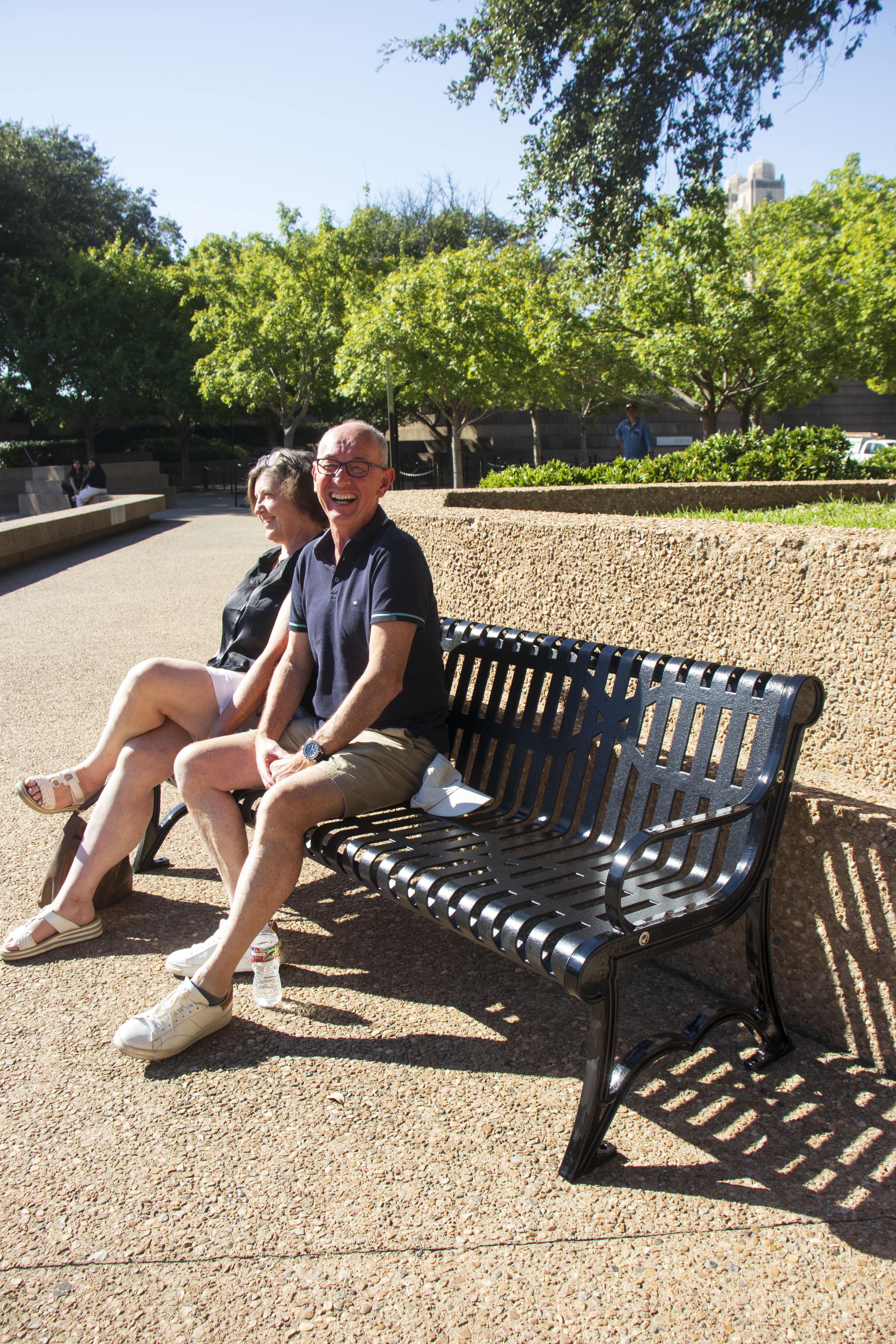 Black MyTCoat Austin Bench Slatted Steel Lifestyle Image with Park Background and Couple Sitting Down