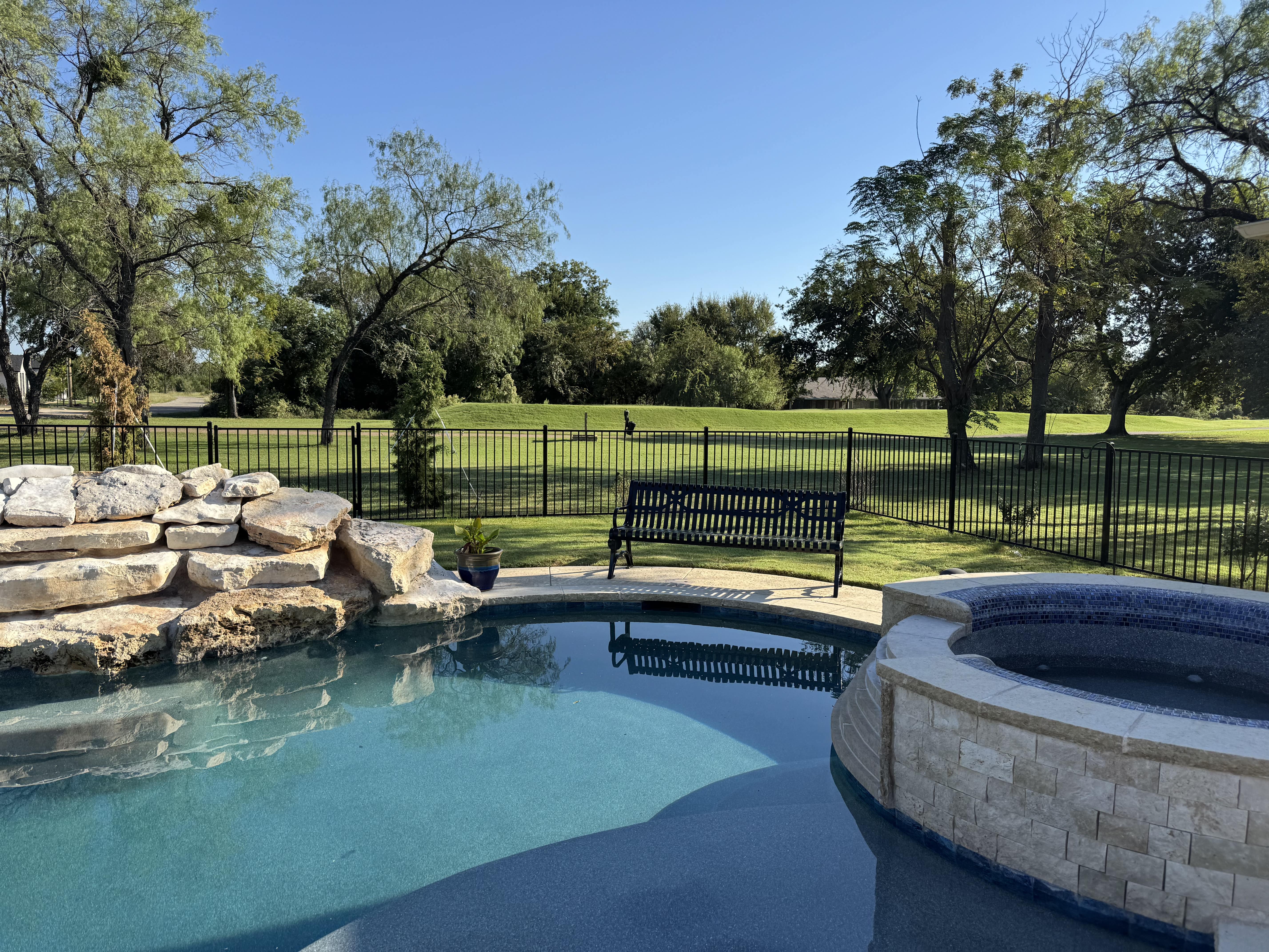 Black MyTCoat Austin Bench Slatted Steel Lifestyle Image with Pool and Golf Course Background