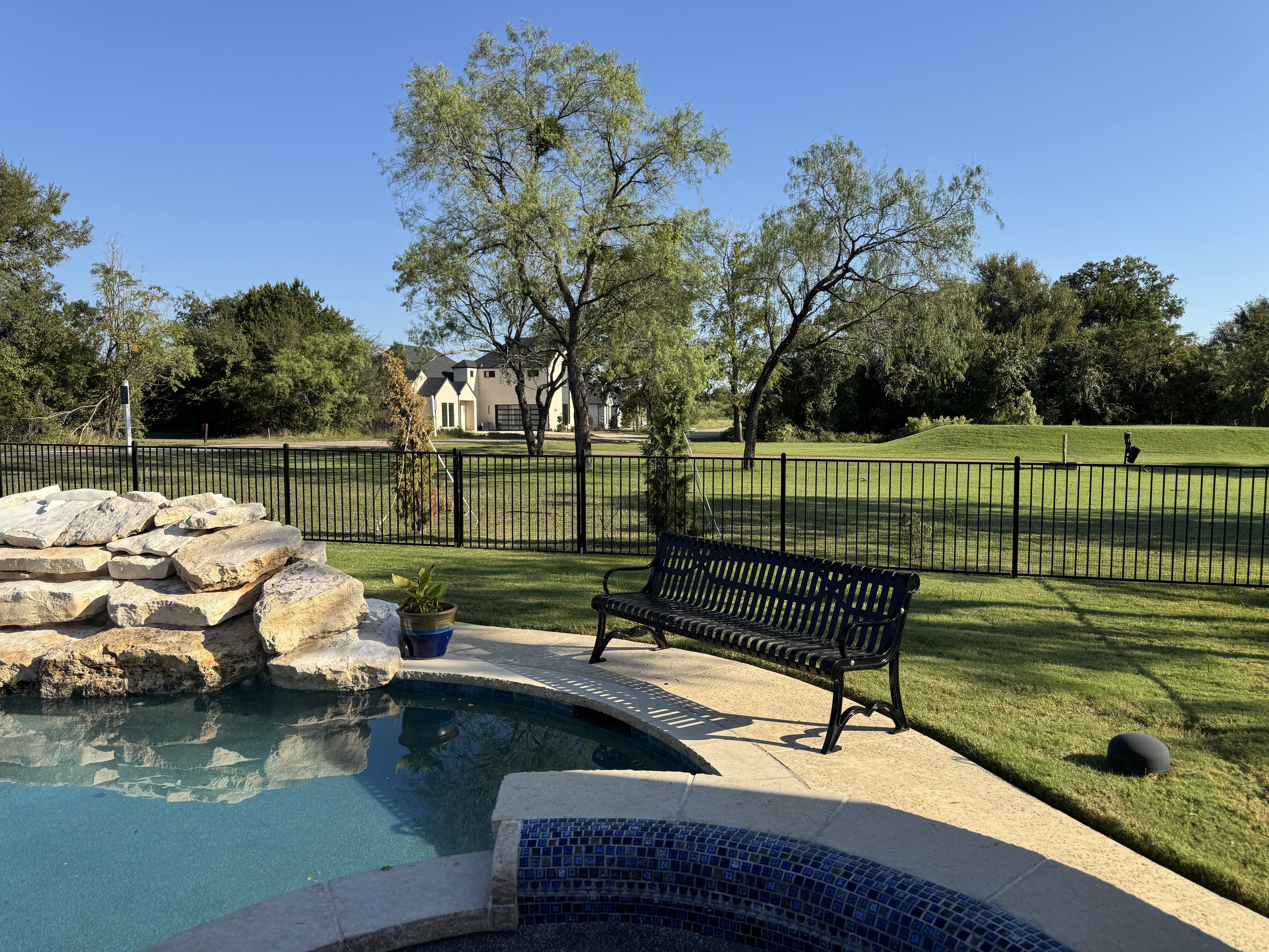 Black MyTCoat Austin Bench Slatted Steel Lifestyle Image with Pool and Golf Course and Large Residential Background