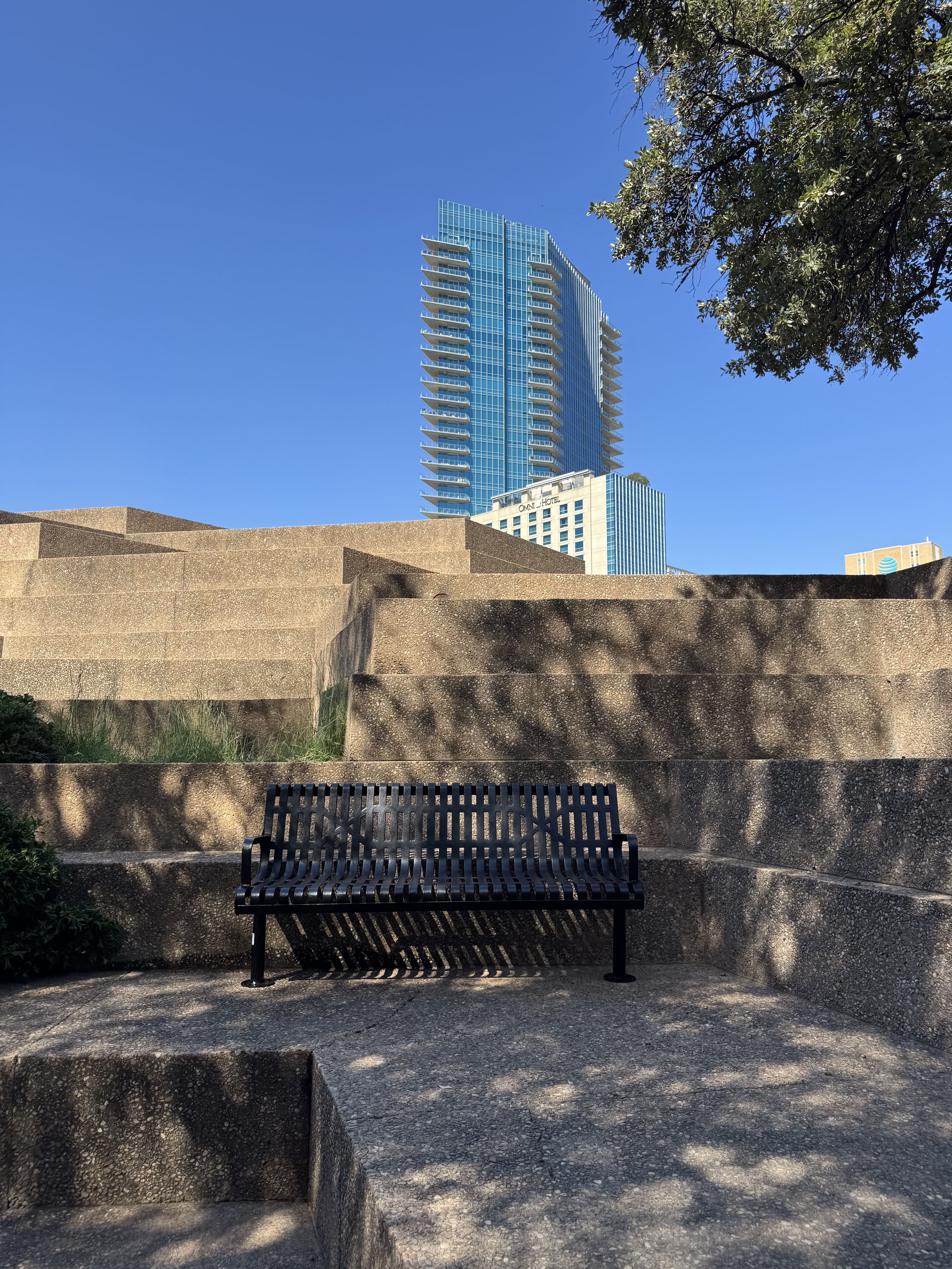 Black MyTCoat Contoured Bench Slatted Steel and Surface Mount Lifestyle Image with City Buildings Background