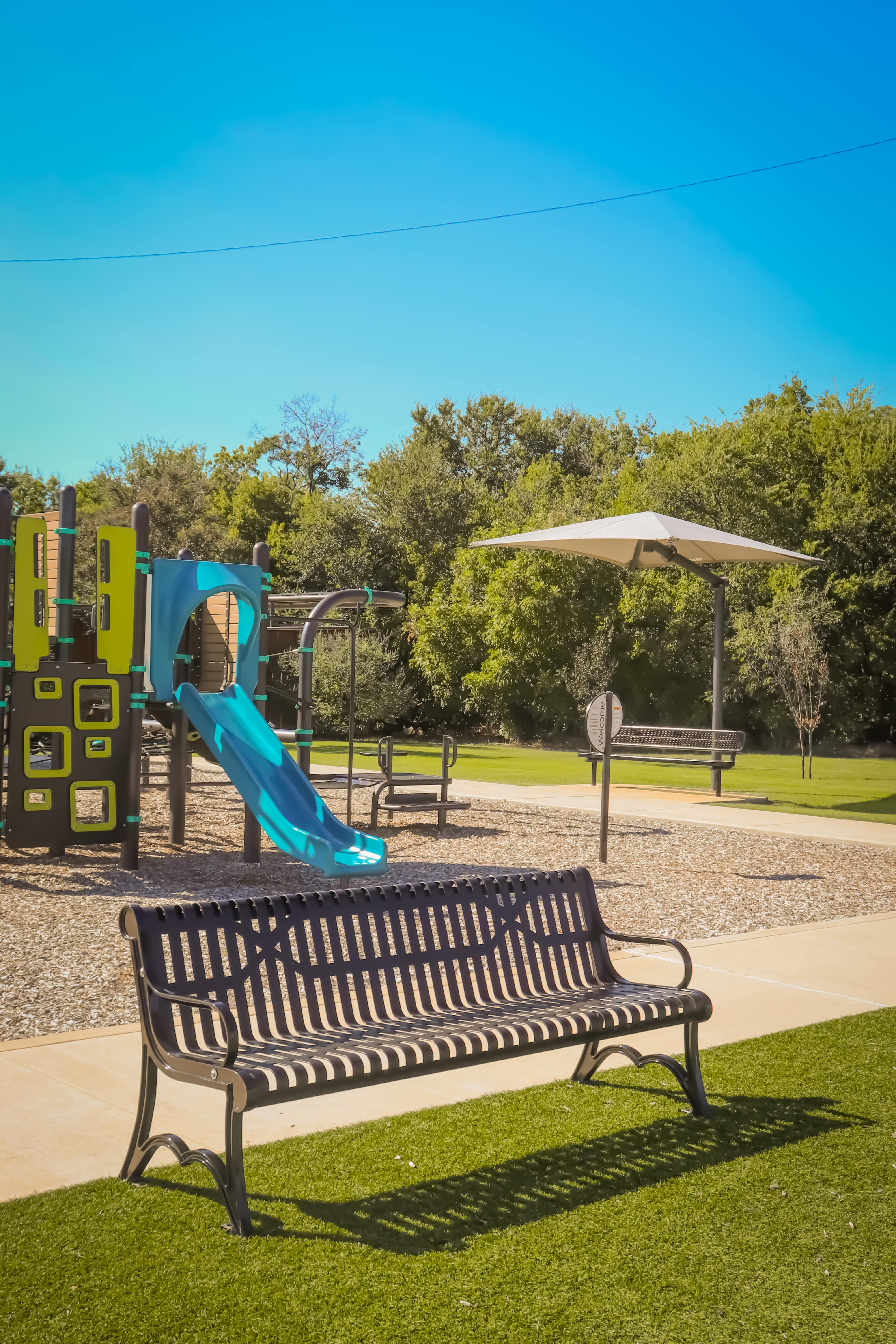 Brown MyTCoat Austin Bench Slatted Steel Lifestyle Image with Playground Background