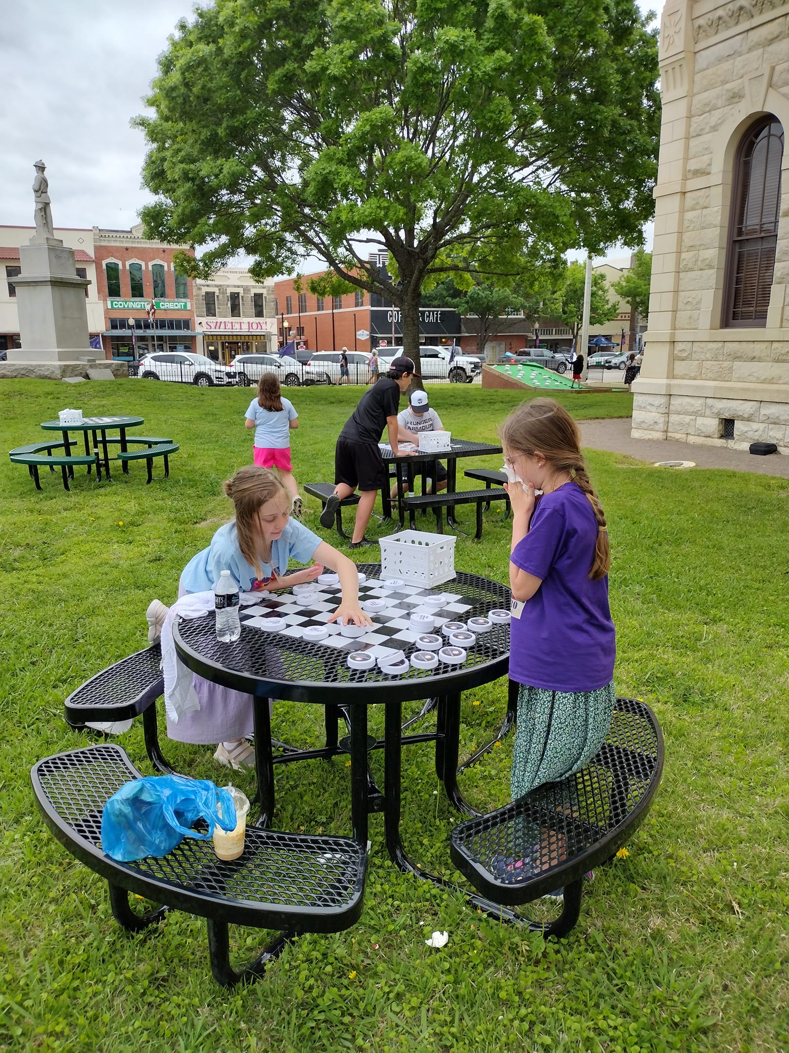 Custom Black MyTCoat Round Portable Picnic Table Lifestyle Image with Kids Playing on Custom Checker Game Board