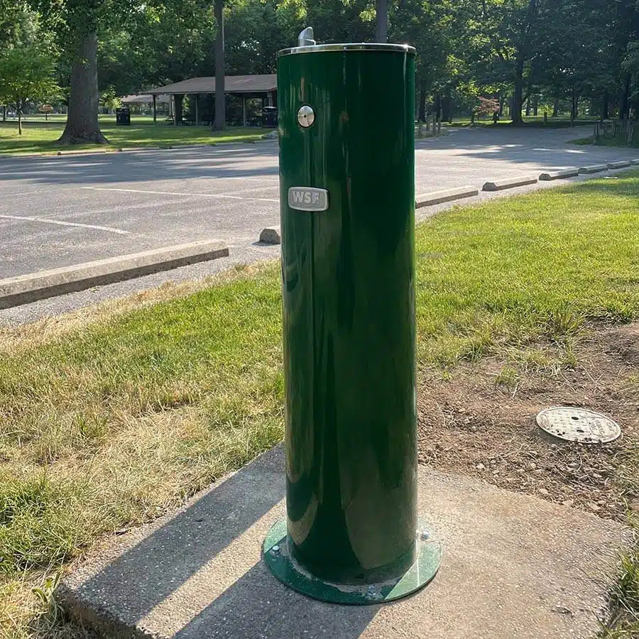 Green Willhoughby Single Outdoor Drinking Fountain on a concrete slab in a park setting Lifestyle Image