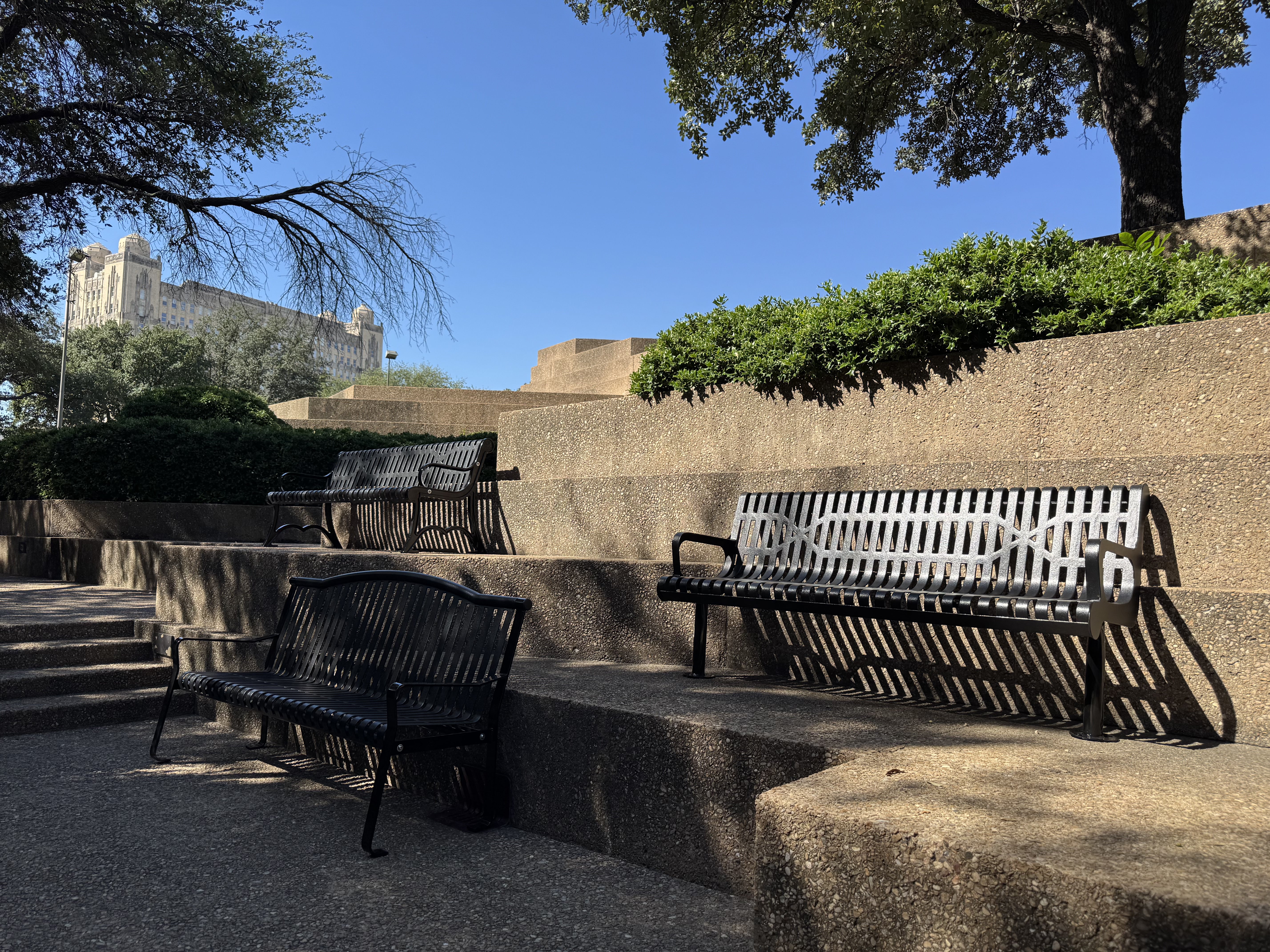 Multiple Black MyTCoat Austin Benches and MyTCoat Contoured Bench Slatted Steel Lifestyle Image with Bush Garden and Building Background