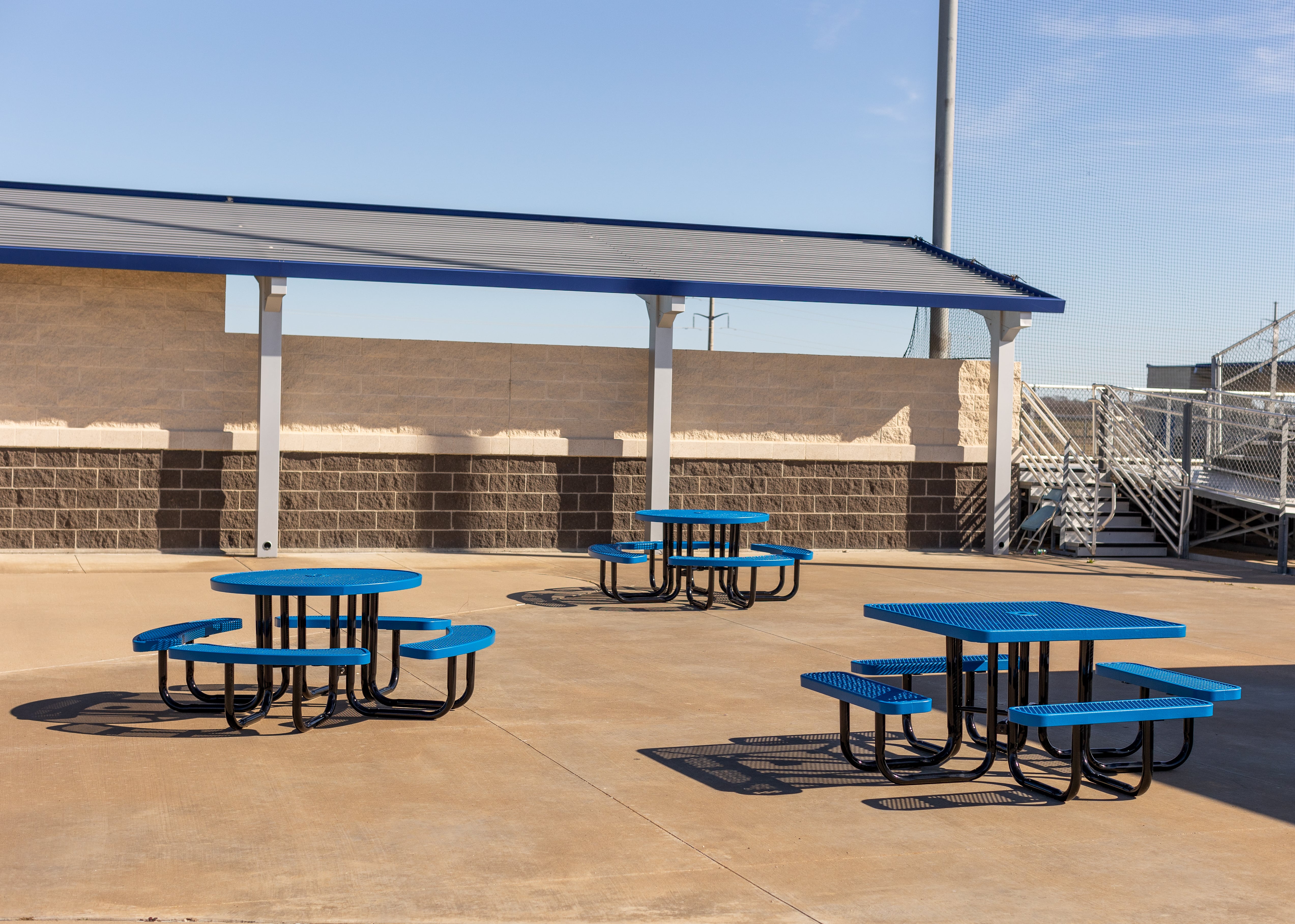Multiple Blue MyTCoat Square Portable Picnic Tables in School with Football Field Bleachers Background