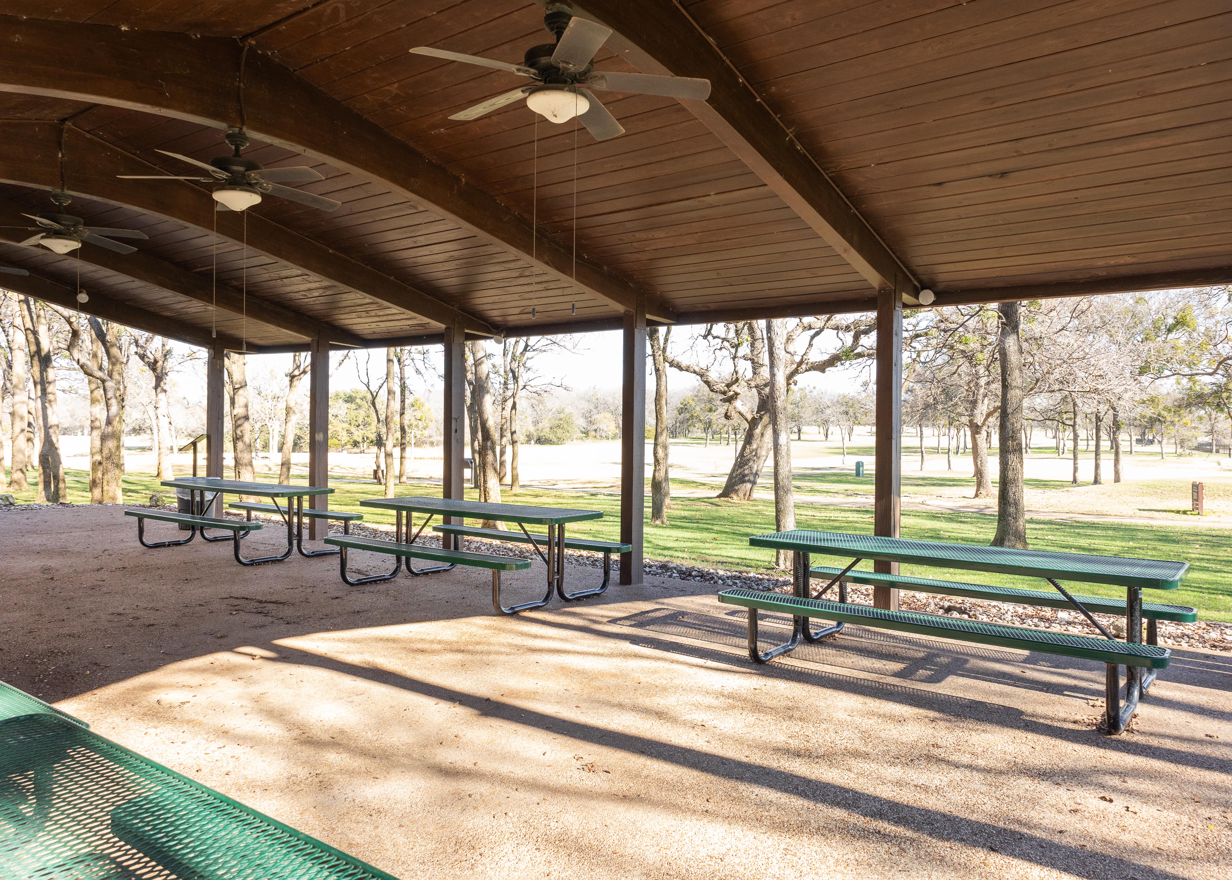Multiple Green MyTCoat Rectangular Portable Picnic Table Under Large Shed with Open Park Background Lifestyle Image