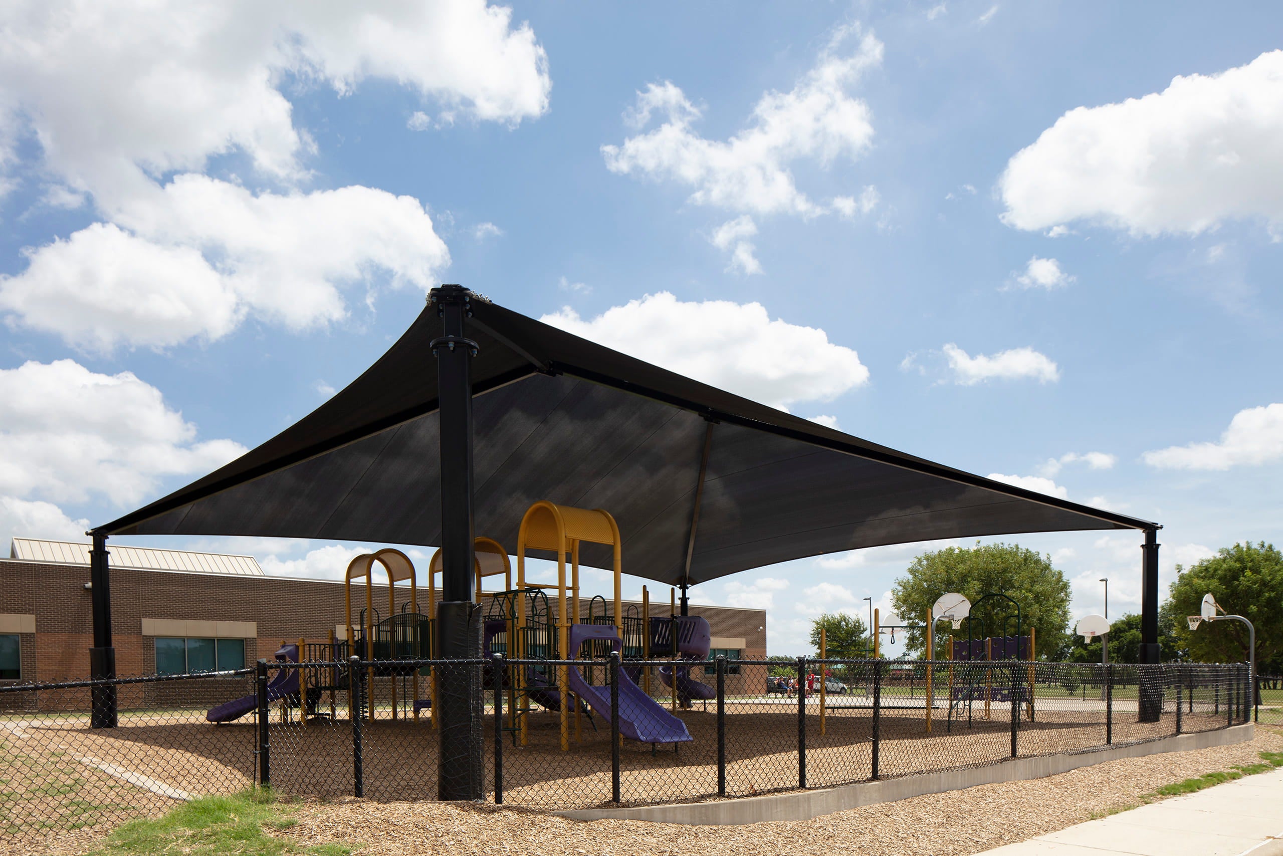 Black USA Shade Super Span Hip over a playground with a blue sky and clouds in the background