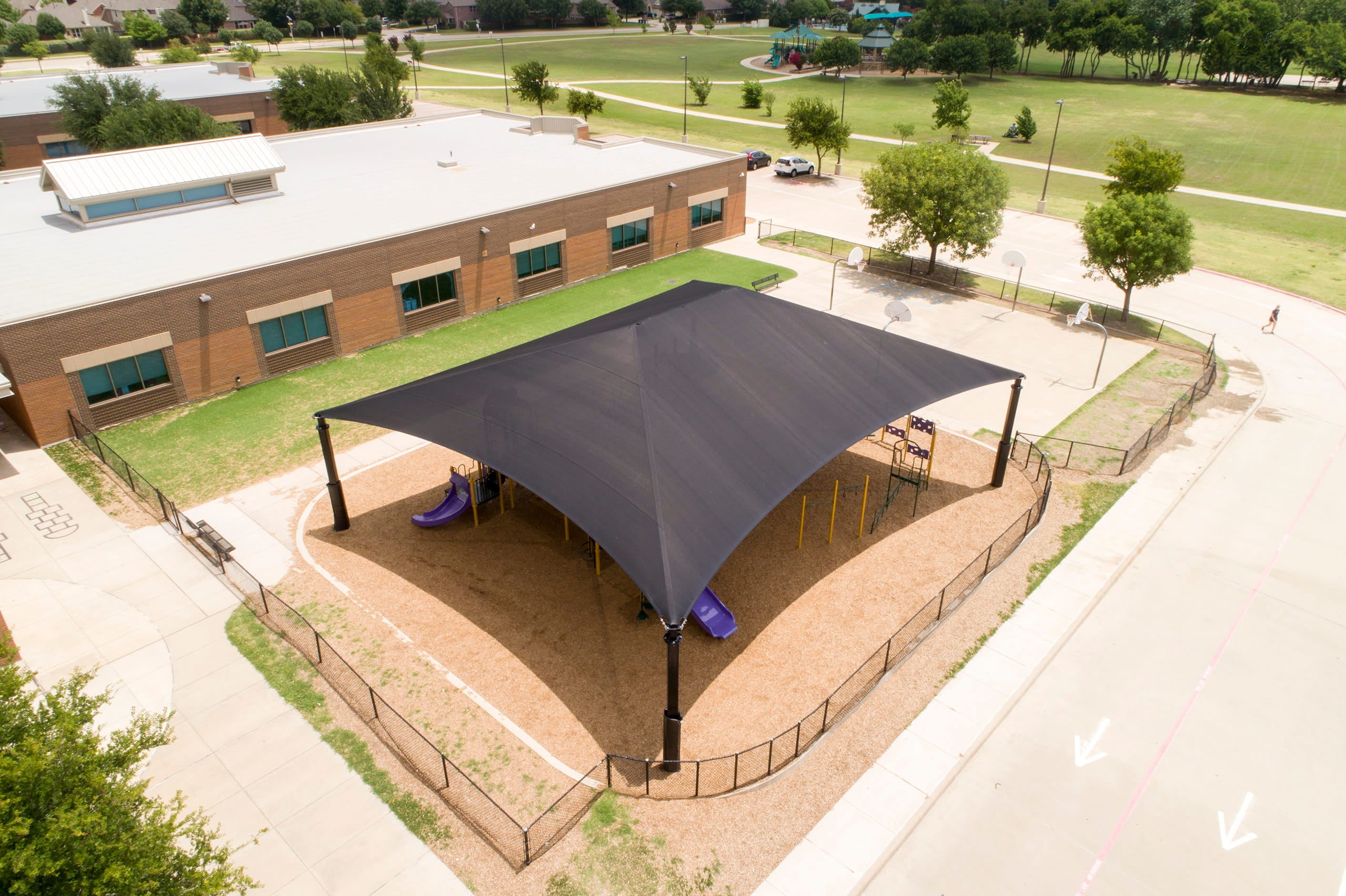 Large black USA Shade Super Span Hip over a playground area in an outdoor setting with a building and trees in the background.