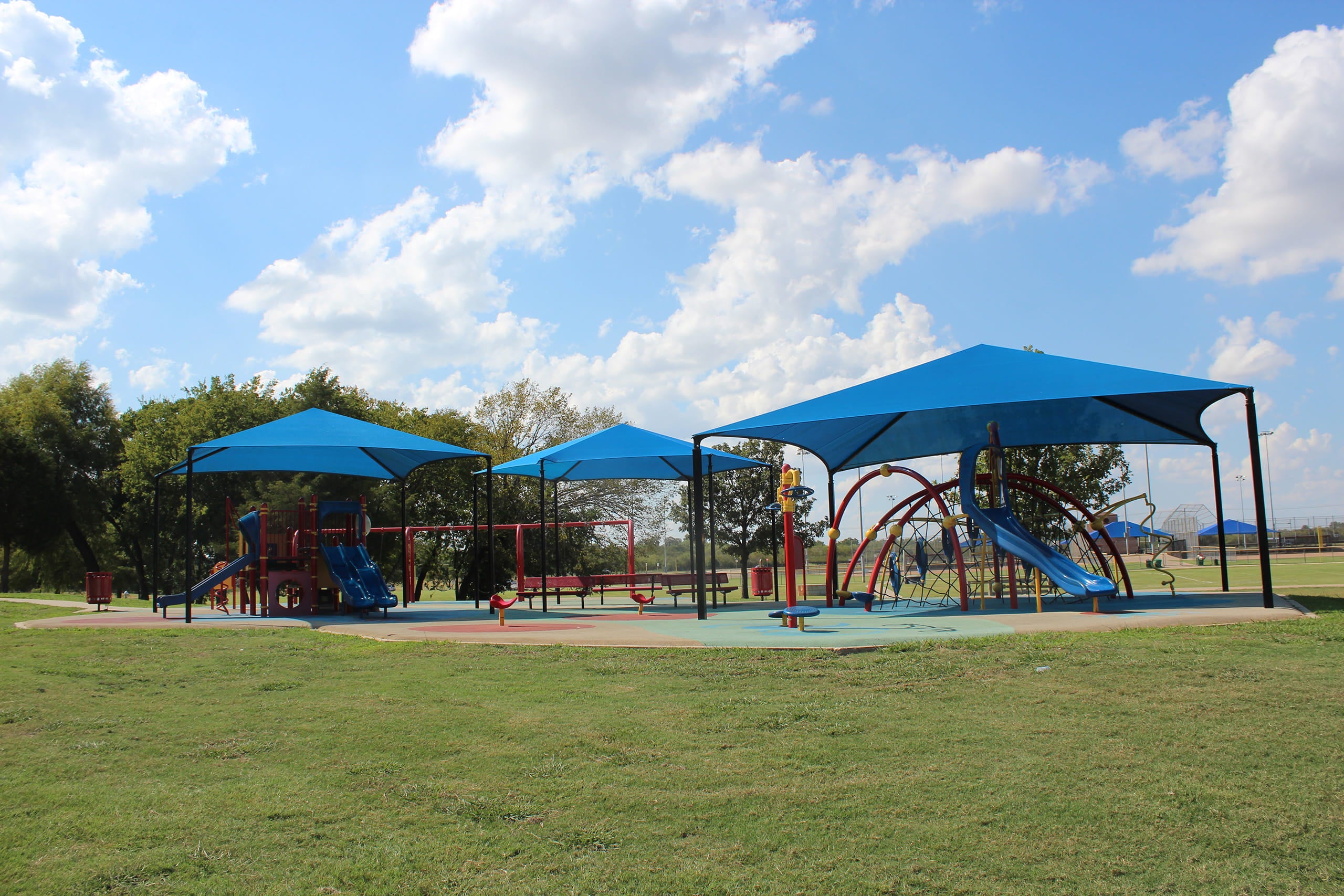 Children's playground with blue USA Shade Hips and slides under a clear blue sky.