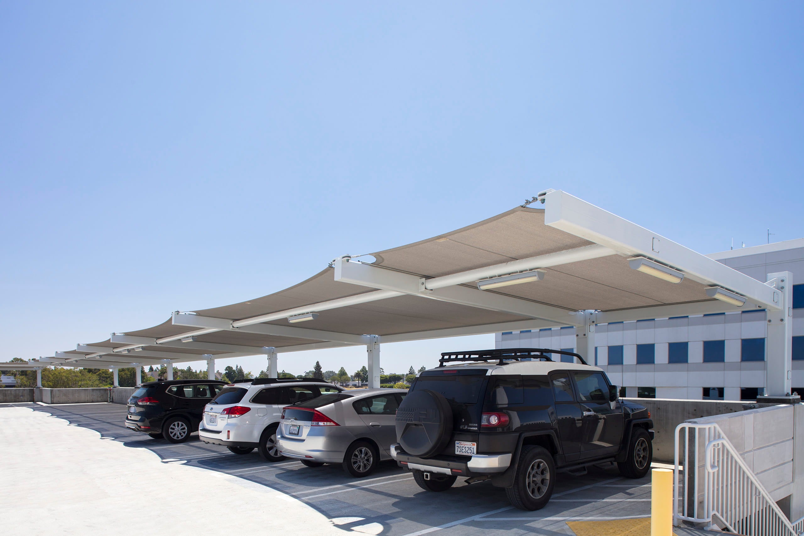 Parking lot with cars under a long USA Shade Slanted Cantilever Cabled on a clear day.