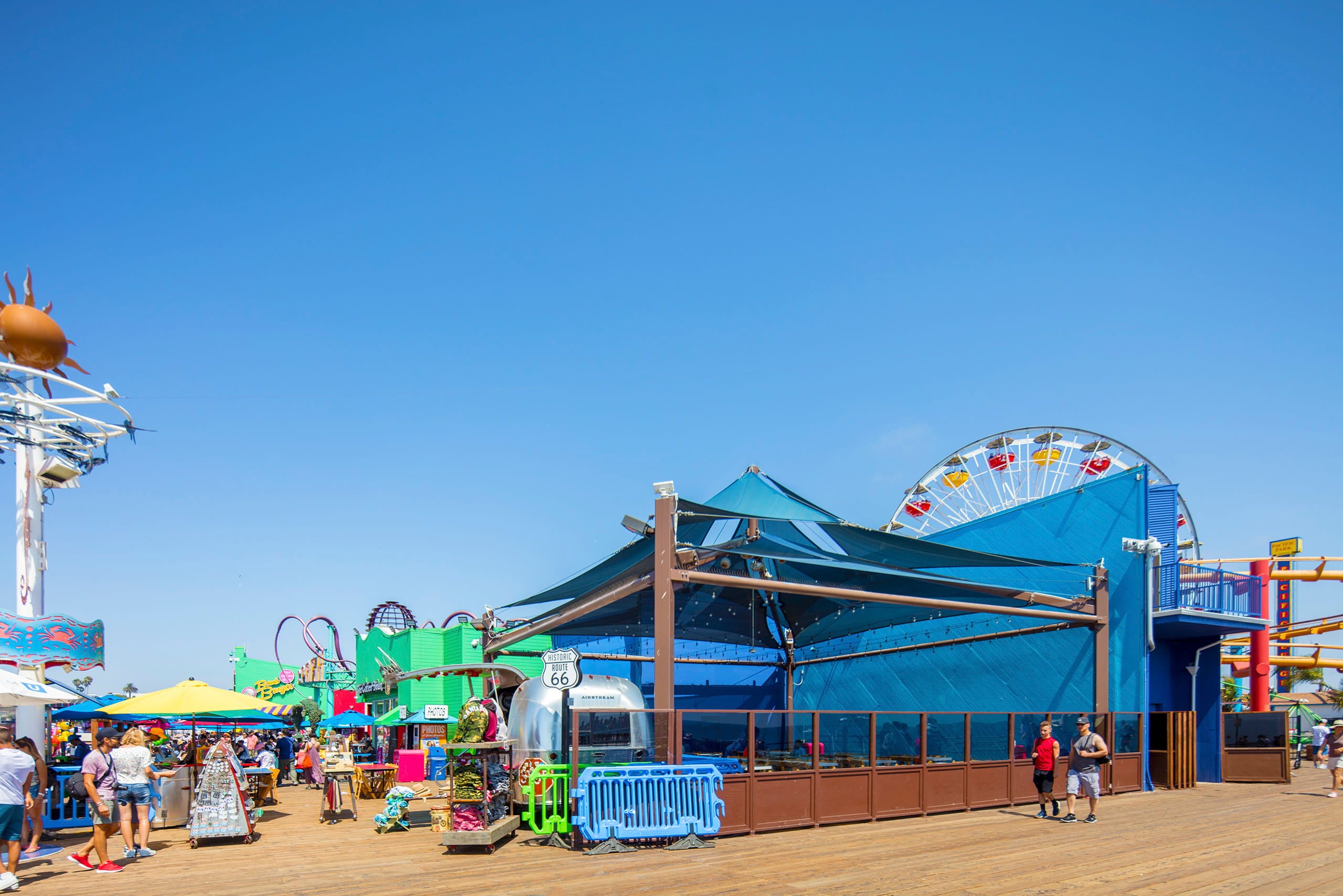 Amusement park with colorful rides and clear blue sky an restaurant with USA Shade Multi-layer Super Span Pyramid Shade covering at santa monica pier