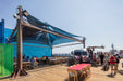 Outdoor seating area with tables and chairs on a wooden deck under a large blue USA Shade Multi-Layer Super Span Pyramid Shade at santa monica pier.