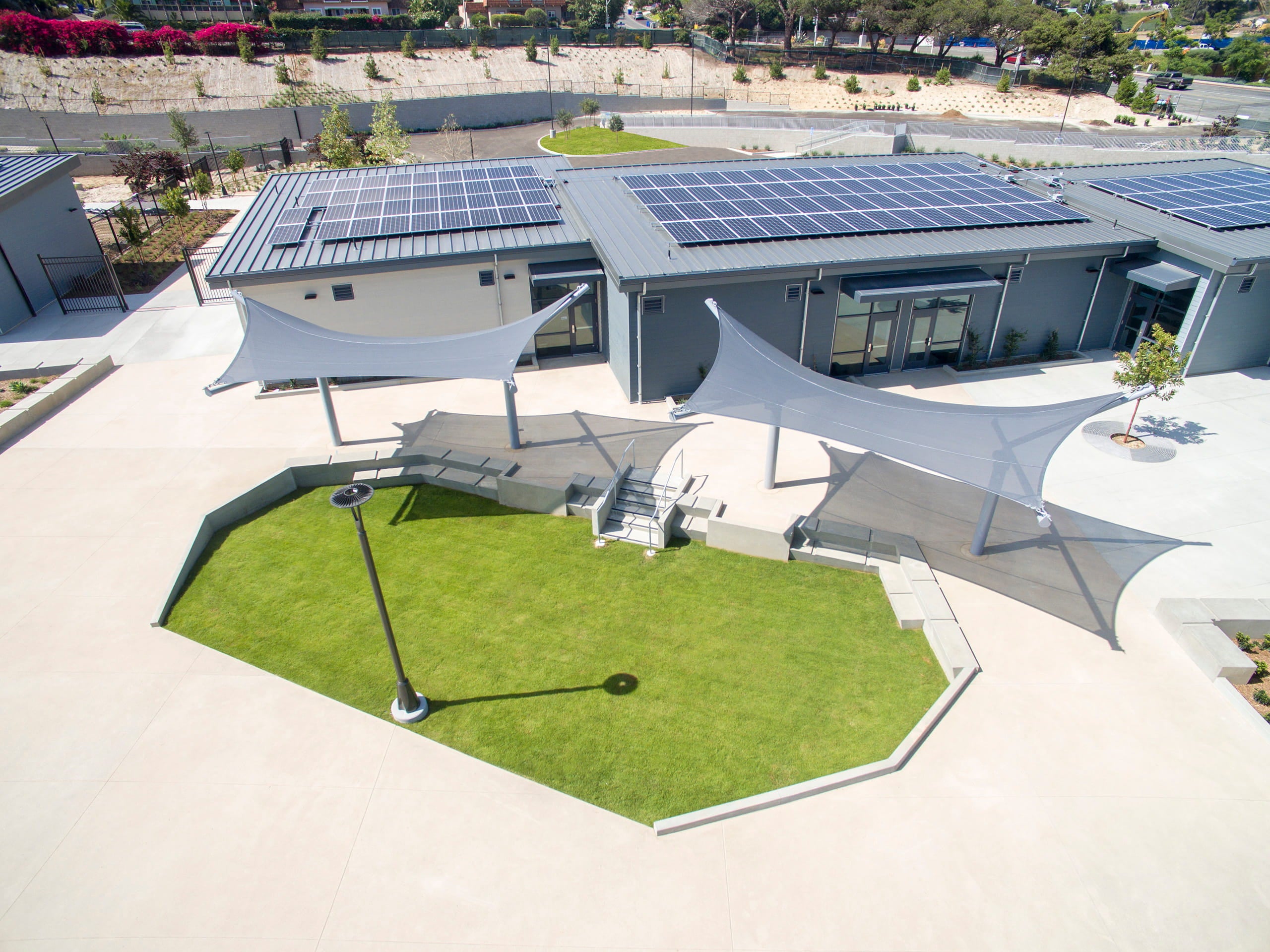 Solar panels on a building with a green lawn and USA Shade Aquarius Shade structures.