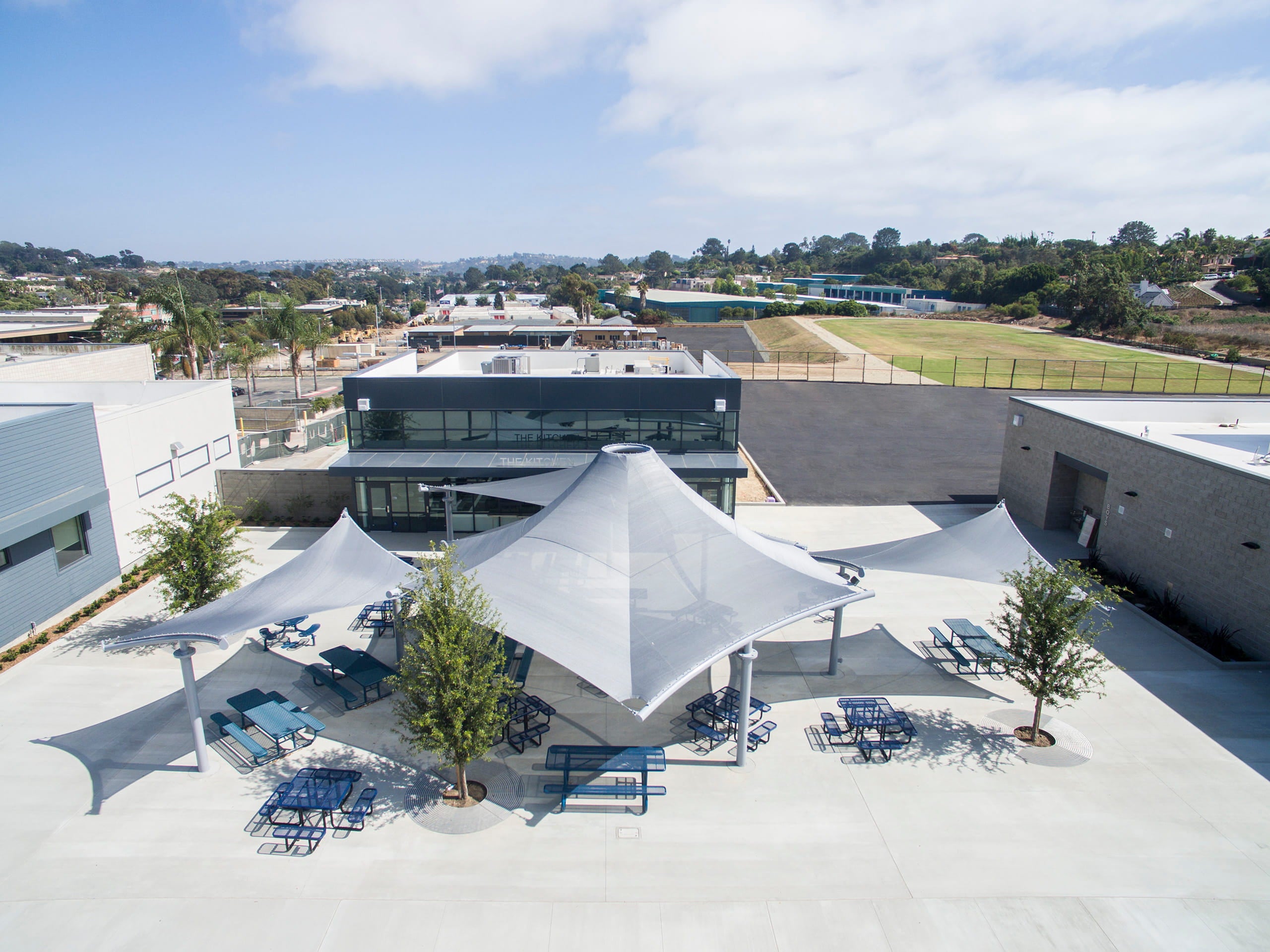 Outdoor area with white umbrellas and USA Shade Orion Shades and tables in front of a modern building with a clear sky.