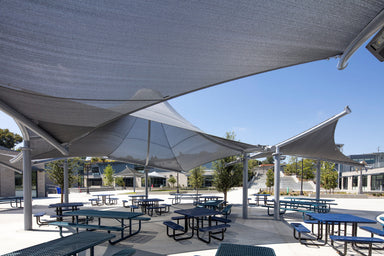 Outdoor seating area with shaded picnic tables under large fabric canopies including USA Shade Orion Shade on a clear day.