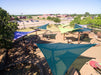 Playground with colorful USA Shade Arbor Shade sails and a view of a parking lot and buildings in the distance.