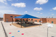 Playground with blue USA Shade Super Span Hip and colorful ground markings under a clear blue sky.