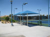 Tennis court with a blue USA Shade Two Post Hip Shade Structure and surrounding area on a clear day.