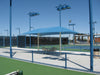 Tennis court with a blue USA Shade Two Post Hip Shade Structure and chairs under a clear blue sky.