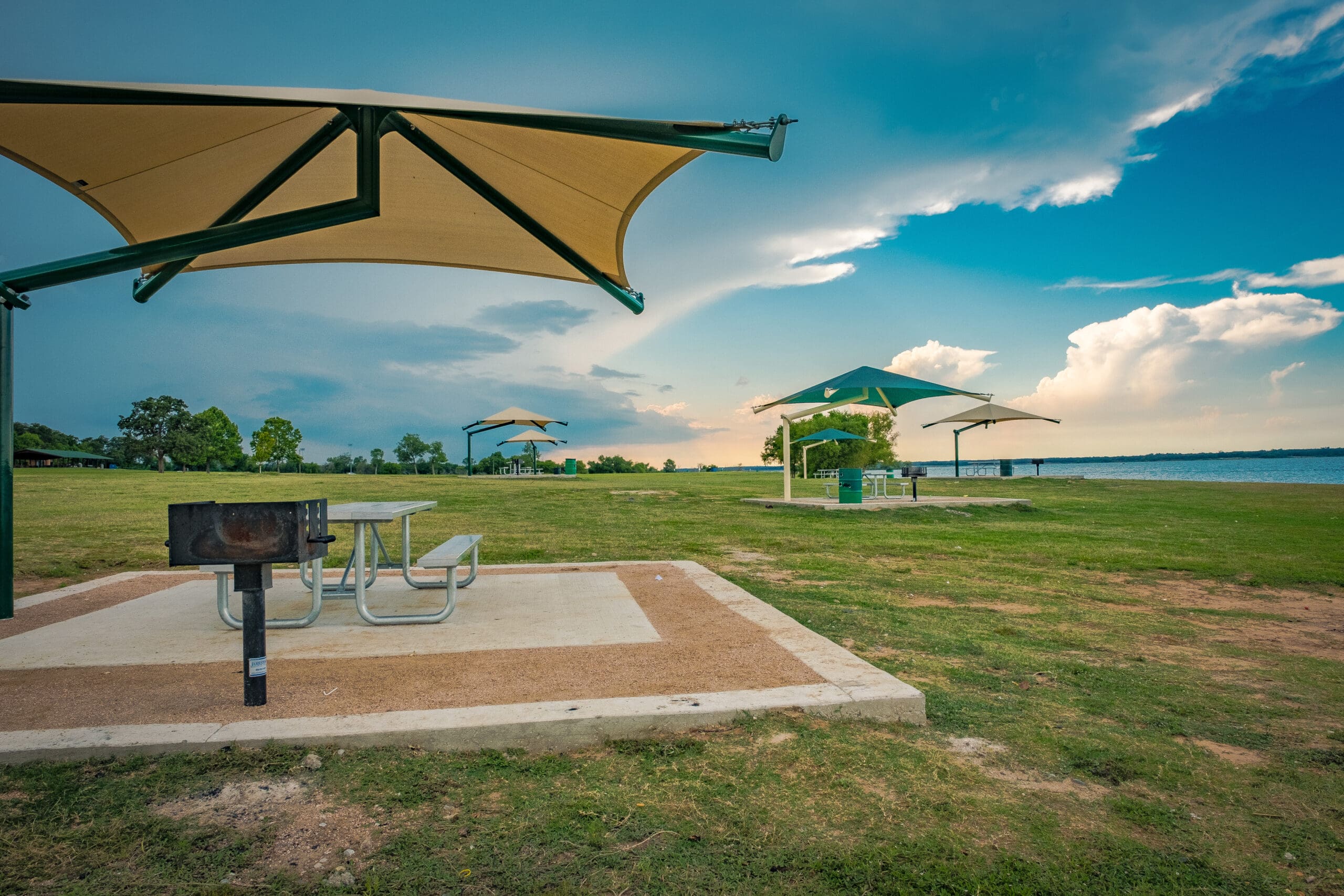 Picnic area with tables, grills, and USA Shade Single Post Cantilever Shade Structures in a park setting.
