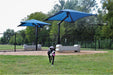 Dog playing in a fenced area with blue USA Shade Single Post Cantilever Shade Structures and large bone-shaped structures.