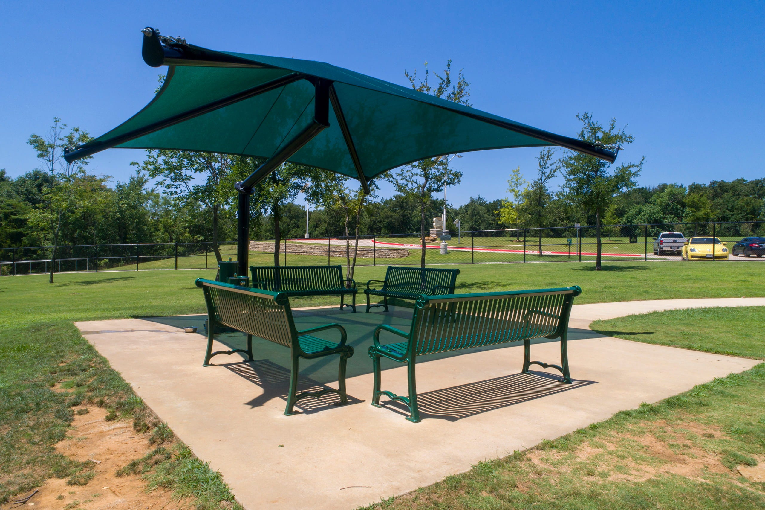 Green outdoor seating area with a large USA Shade Single Post Cantilever Shade Structure in a park setting