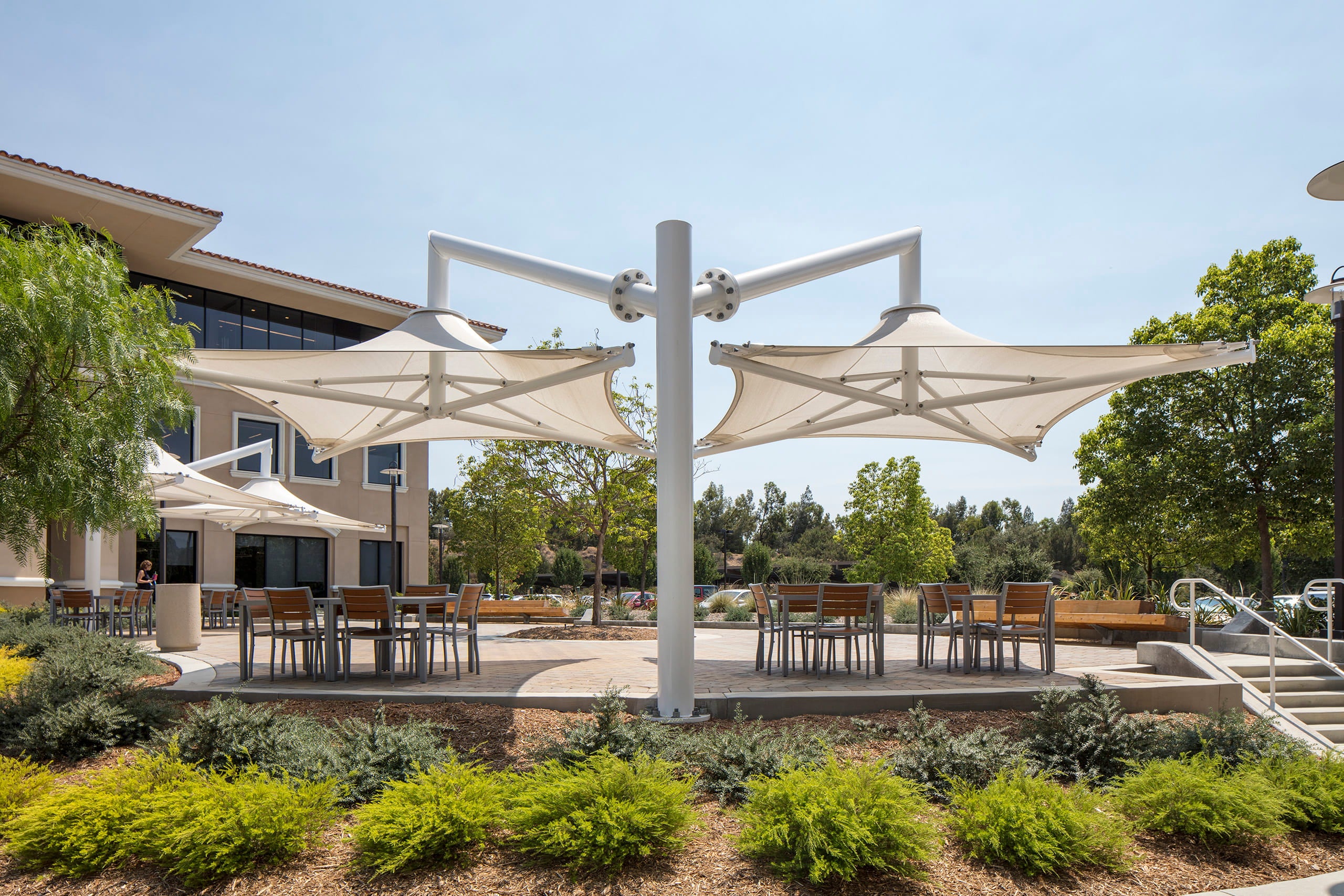 Outdoor seating area with large USA Shade Solana Cantilevers and tables in a park-like setting.