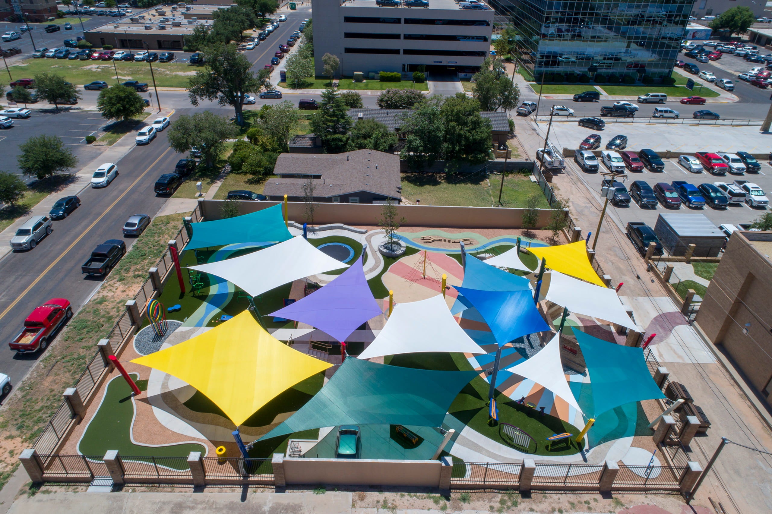 Colorful 4-point hypar shade sails over a playground area at recreational center in an urban setting