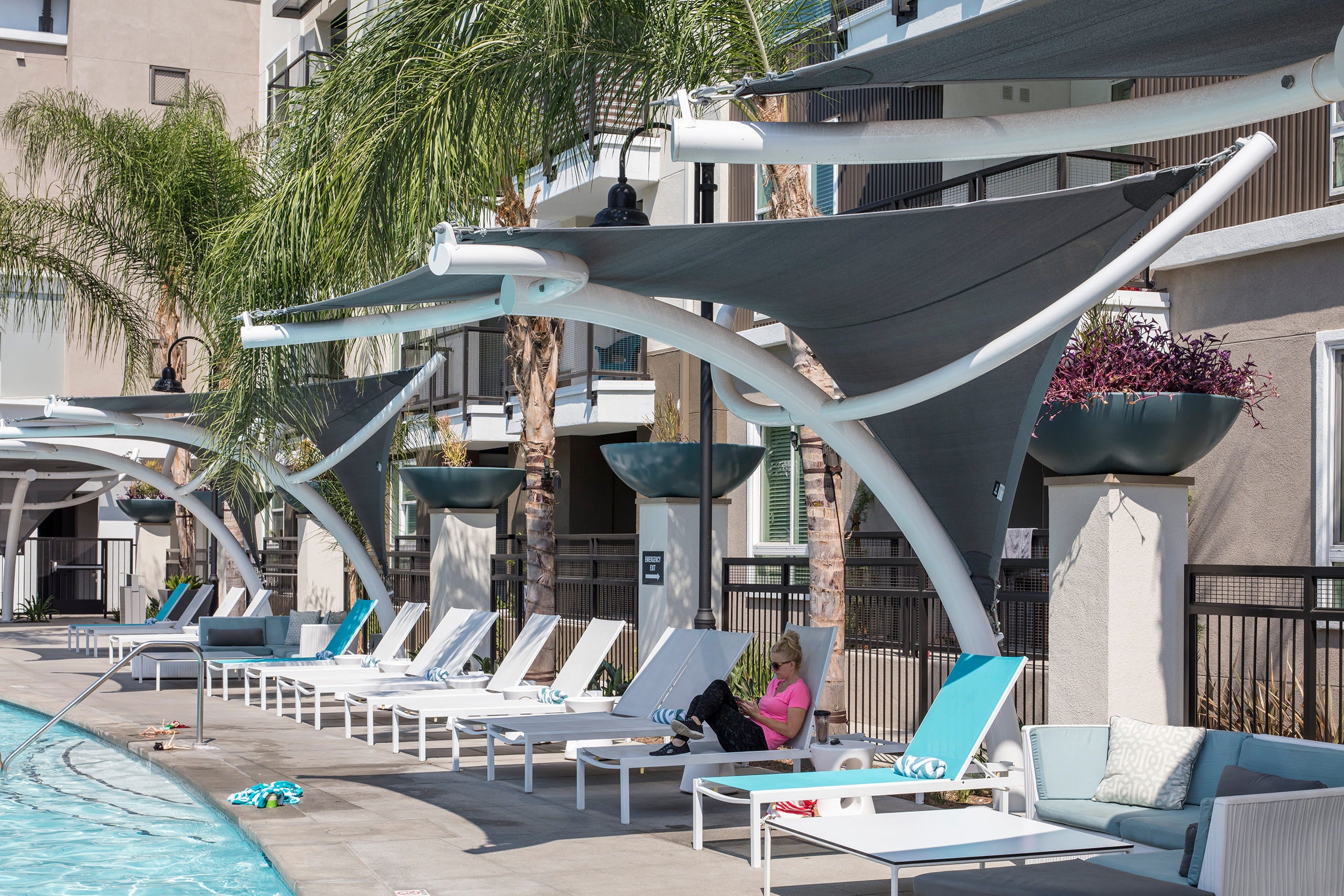 Poolside area with lounge chairs, USA Shade Pegasus Shades, and a person reading a book under.