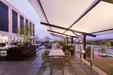 Outdoor patio area with tables, chairs, under a USA Shade Slanted Cantilever Cabled and a building in the background