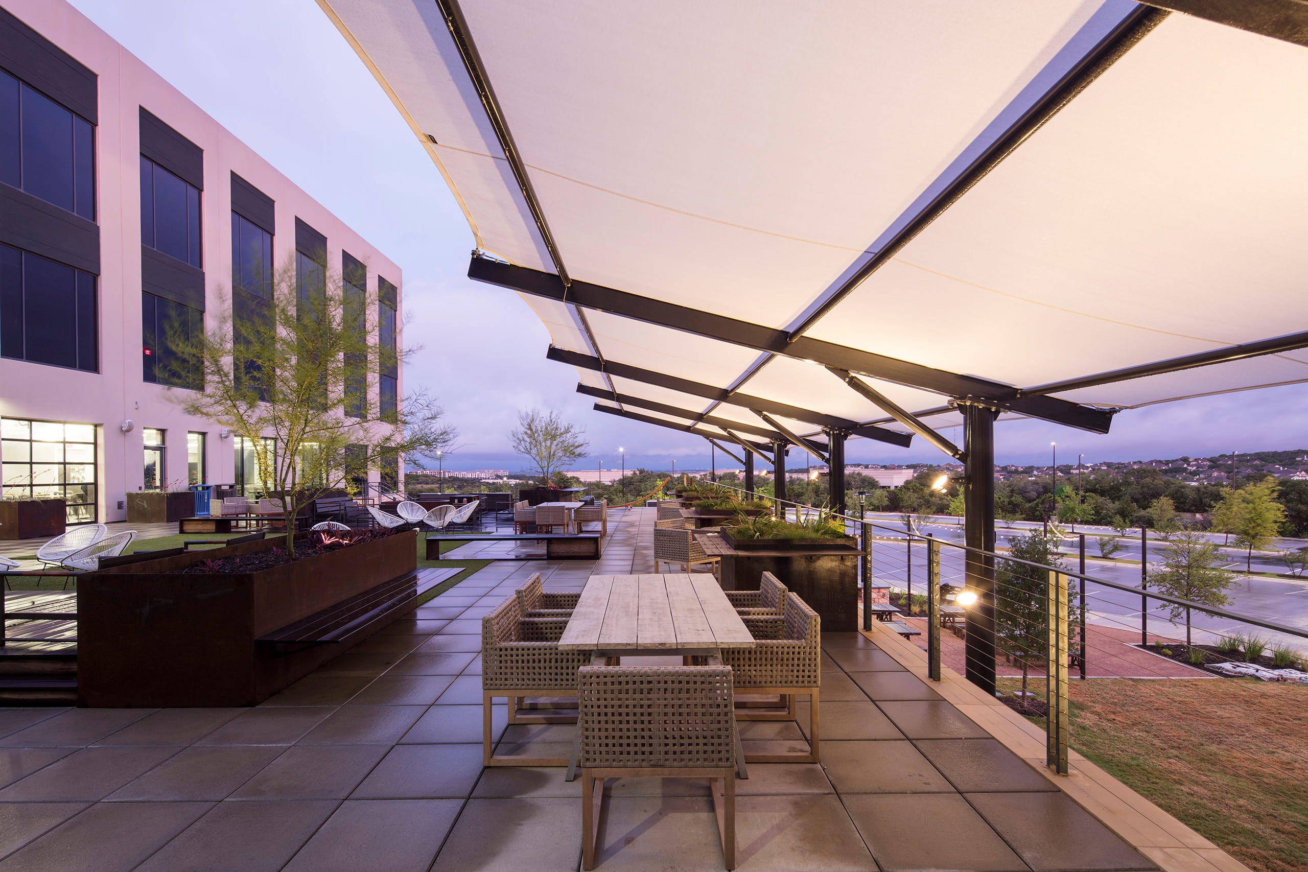 Outdoor patio area with tables, chairs, under a USA Shade Slanted Cantilever Cabled and a building in the background