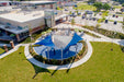 Aerial view of a park with a large blue shade 4-point hypar Sail structure and surrounding greenery at recreation center.