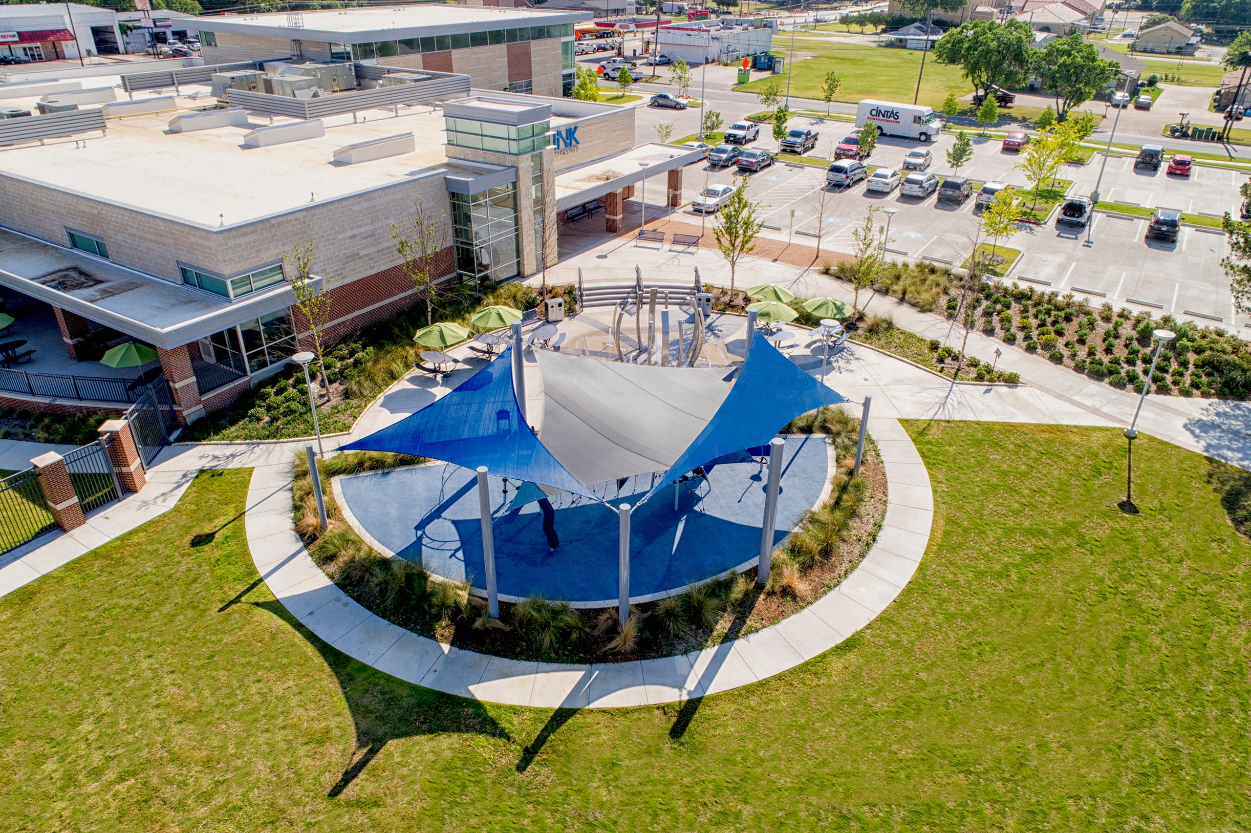 Aerial view of a park with a large blue shade 4-point hypar Sail structure and surrounding greenery at recreation center.