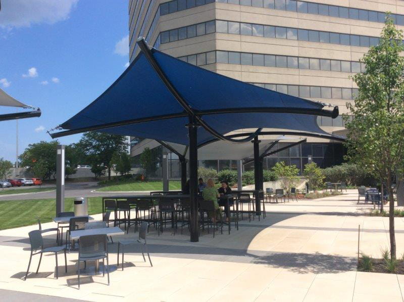 Outdoor seating area with blue USA Shade Aquarius Shade in front of a building