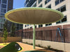 Round USA Shade Cantilever Disc Shade structure with a green frame and beige Fabric in an urban setting.