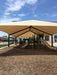Playground with slides and climbing structures under a large beige USA Shade Super Span 6-Post Hip on a sunny day.