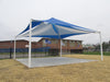 Blue and white USA Shade Mariner Pyramid Shade structure on a grassy area with a building in the background