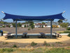 Blue USA Shade Aquarius Shade structure over picnic tables in a park setting with houses in the background.