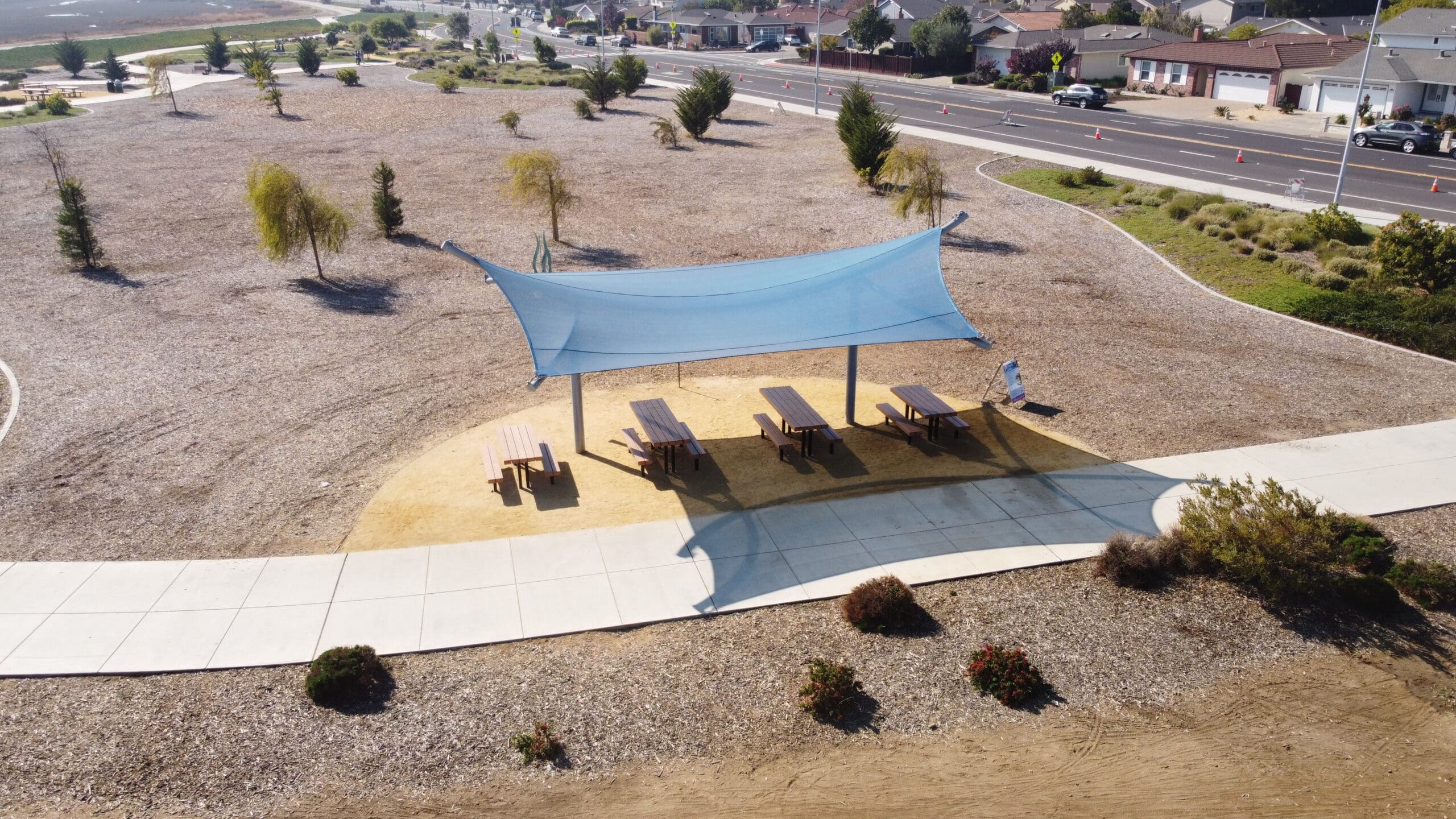 A large blue USA Shade Aquarius Shade sail over a picnic area with tables and chairs in an open space.