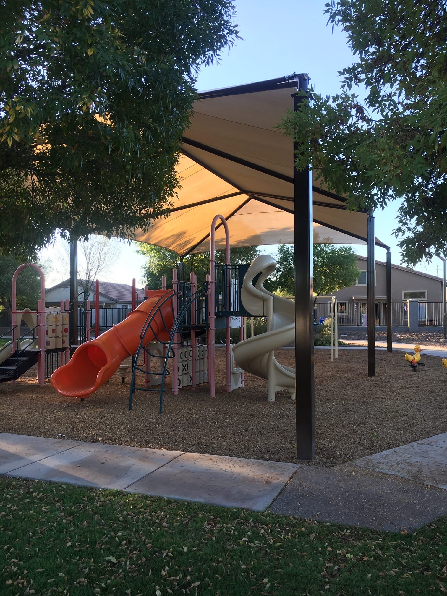 Playground with slides and a large USA Shade Super Span 6-Post Hip providing shade