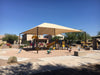 Children's playground with a large beige USA Shade Hip structure on a clear day.