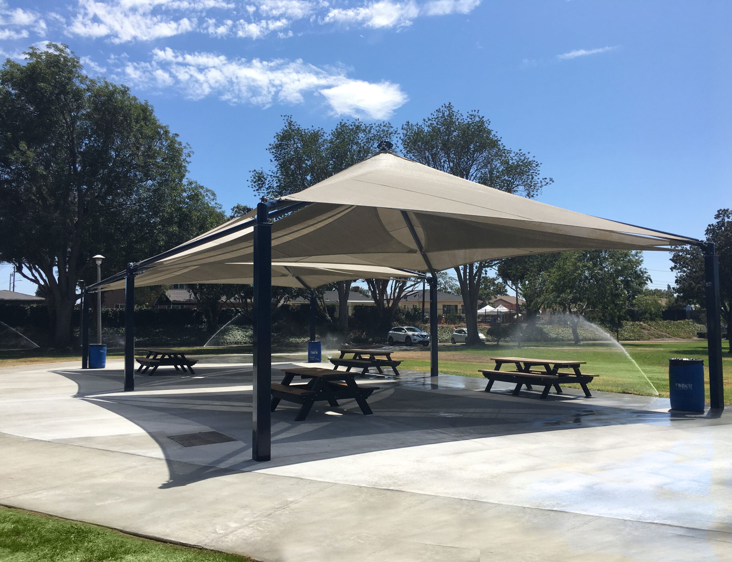 Large outdoor USA Shade Mariner Pyramid Shade providing shade over picnic tables in a park setting.