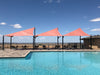 Pool area with pink USA Shade Wave Shades and outdoor furniture under a clear blue sky.