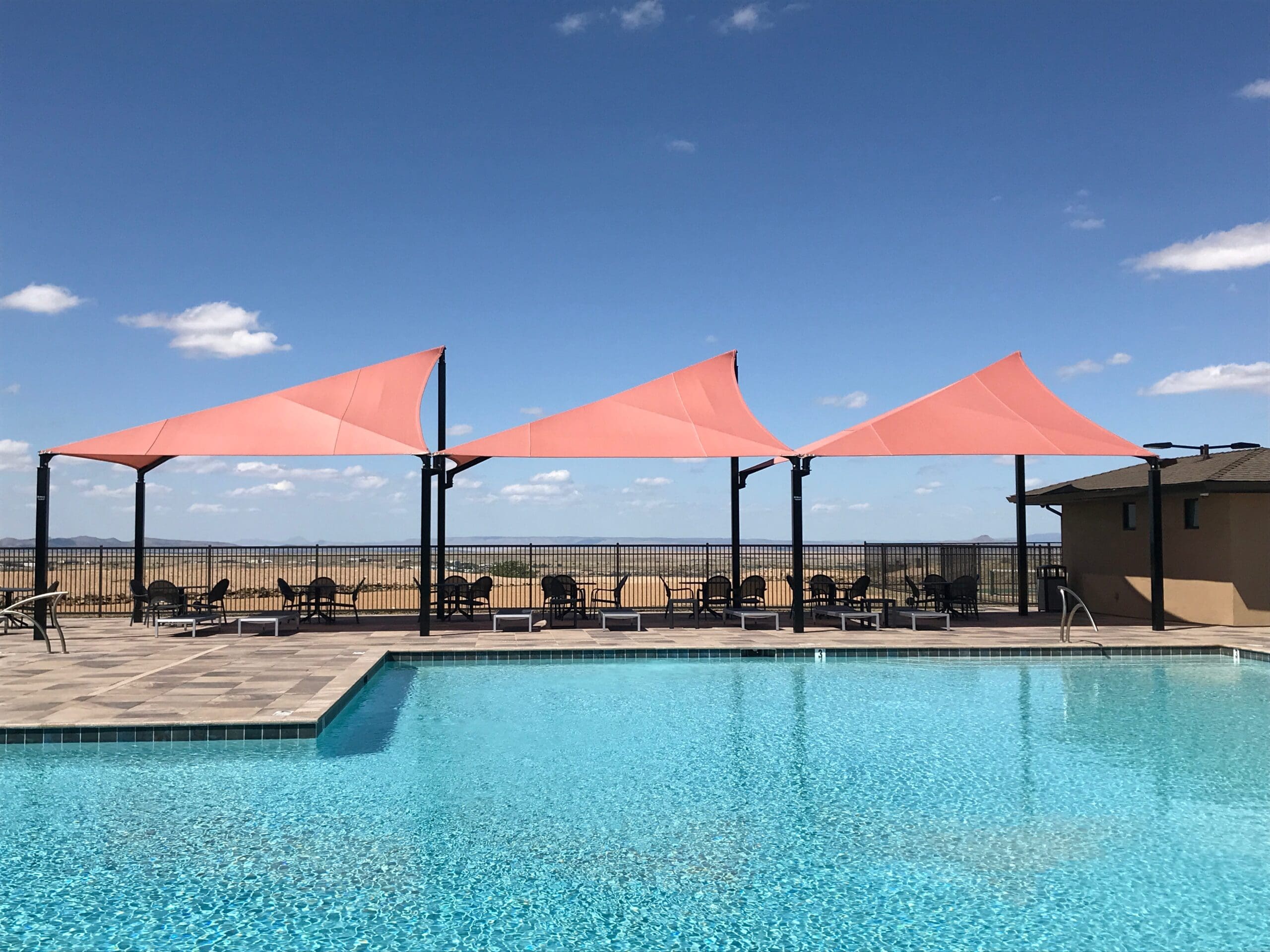 Pool area with pink USA Shade Wave Shades and outdoor furniture under a clear blue sky.