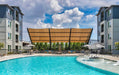Pool area with lounge chairs, USA Shade Slanted Cantilever Cabled, and apartment buildings in the background