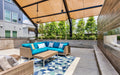 Outdoor patio with blue cushioned sofa, patterned rug, and grill area under a USA Shade Slanted Cantilever Cabled.