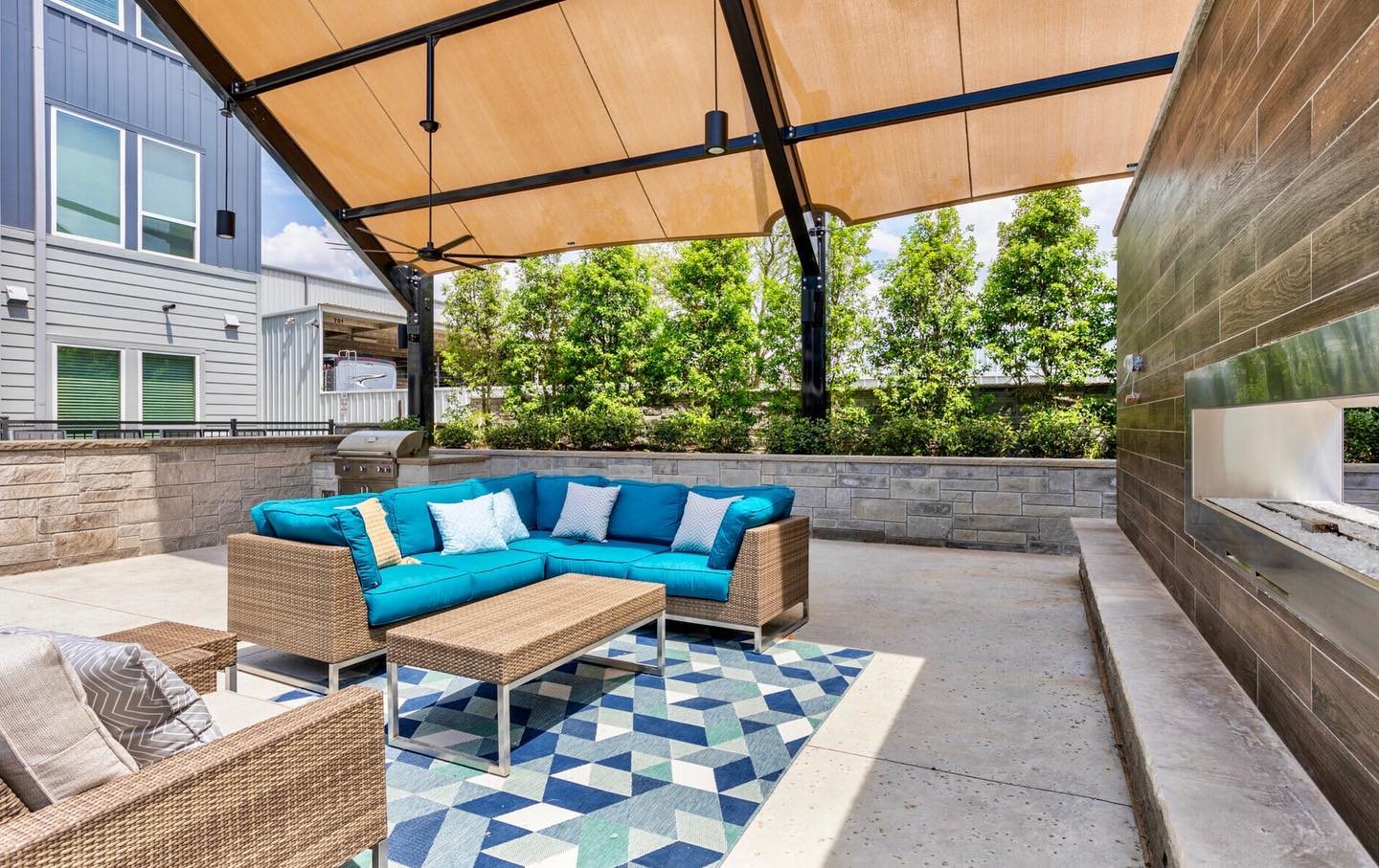 Outdoor patio with blue cushioned sofa, patterned rug, and grill area under a USA Shade Slanted Cantilever Cabled.