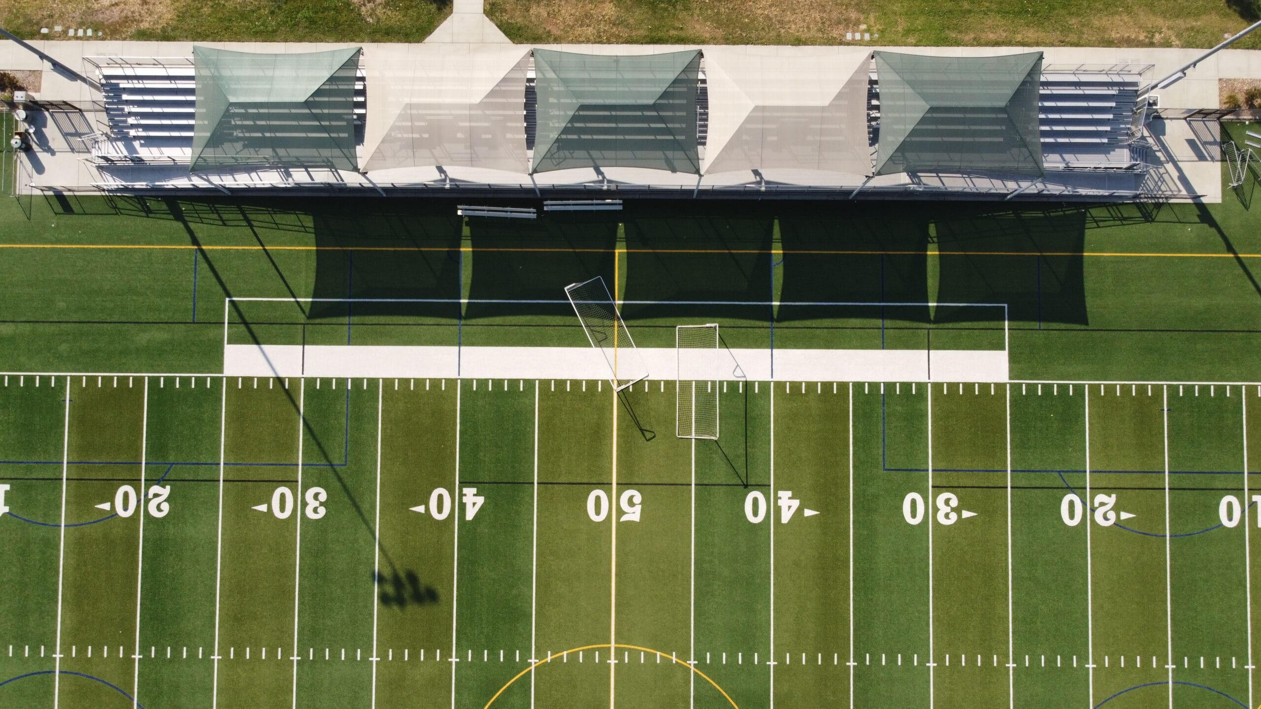 A football field with a stadium seating area covered by USA Shade Hips in the background