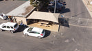 Aerial view of a USA Shade Two Post Hip Shade Structure covering outdoor area with cars parked around it.