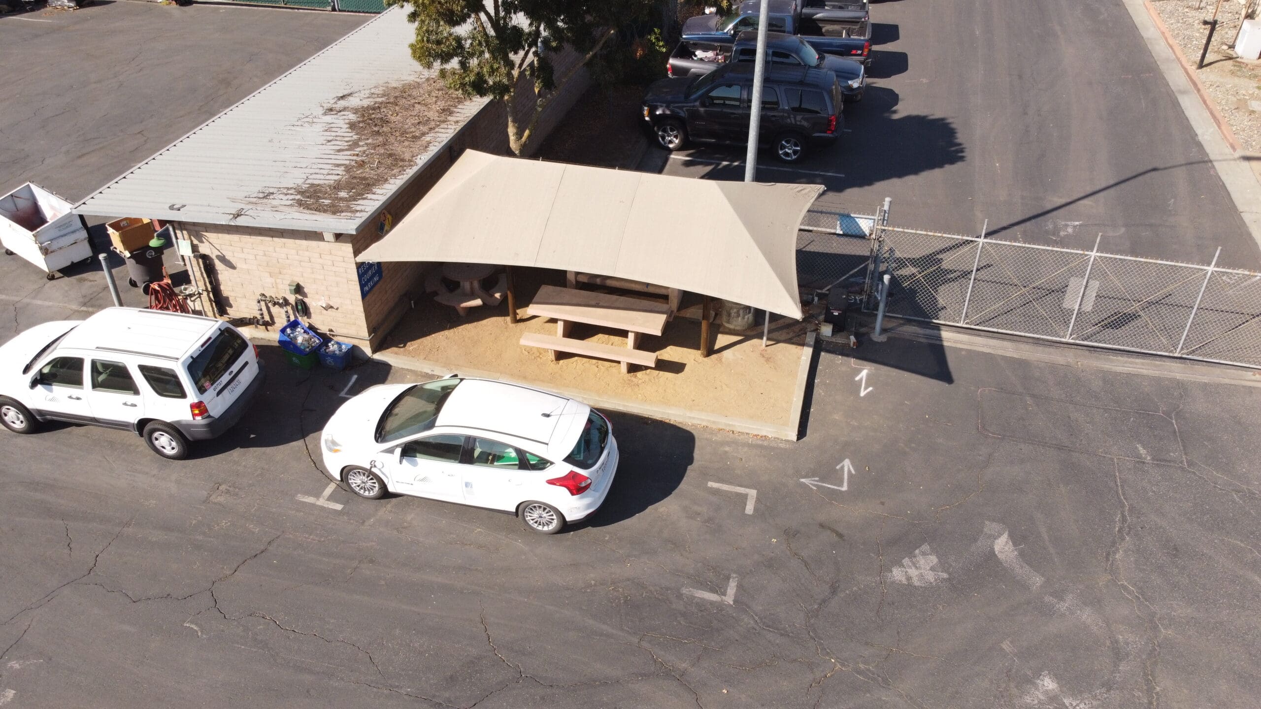 Aerial view of a USA Shade Two Post Hip Shade Structure covering outdoor area with cars parked around it.